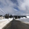 Route enneigée avec maisons qui bordent la route et montagnes au loin.