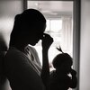 Silhouette d'une femme qui a son jeune enfant dans les bras, adossée contre le mur, dans un couloir. Elle se touche le front comme si elle avait mal à la tête.