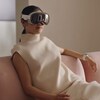 Une femme est assiste sur un canapé rose, et porte un casque de réalité virtuelle. 