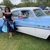 Une femme est costumée dans les années 50 avec une voiture tout droit sortie de cette époque. 
