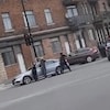 Des policiers retranchés derrière une voiture pointent leurs armes vers un autre véhicule.