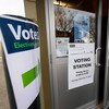 Un homme ouvre une porte où est posée une affiche indiquant qu'il s'agit d'un bureau de vote.