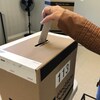 La main d'une personne qui dépose un bulletin de vote dans une boîte officielle d'Élections Québec.