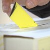 Une main dépose dans la fente d'une boîte de scrutin un bulletin de vote jaune plié en trois parties.