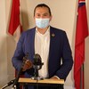 Wab Kinew est debout à un lutrin devant un micro et porte un masque.