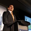 Wab Kinew sourit devant un podium. 