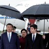 Gabriel Attal et Xi Jinping, côte à côte et suivis de Peng Liyuan, marchent sur un tarmac entourés de gens qui tiennent des parapluies. 