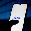 Une personne tient un téléphone intelligent qui affiche le logo de l'application Zoom.