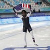 Erin Jackson fait le tour de la patinoire avec un drapeau américain au-dessus de sa tête.