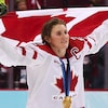 La joueuse porte le drapeau du Canada au dessus de sa tête et sa médaille d'or au cou.