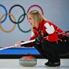 Jennifer Jones penchée vers les pierres de curling et qui regarde au loin pour donner des directives à ses coéquipières. 