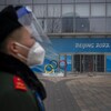 Un garde de sécurité avec un masque et une visière se tient devant un bâtiment olympique à Pékin.