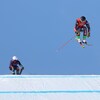 Des skieurs font une course, le premier d'entre eux est dans les airs et effectue un saut.