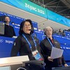 Une femme et un homme avec des vestes noirs et des casques d'écoute décrivent l'action depuis la tribune réservée aux médias