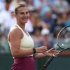 Une joueuse de tennis tient sa raquette dans une main et sourit après avoir remporté un match.