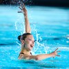 Audrey Lamothe dans la piscine en train de performer, avec le bras gauche levé vers le haut, le bras droit tendu vers l'avant et un grand sourire.