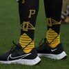 On aperçoit les mollets d'un joueur de baseball, qui porte des bas longs aux couleurs des Pirates de Pittsburgh.