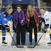 Deux femmes effectuent une mise au jeu protocolaire aux côtés de deux hockeyeuses.