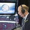 Un homme âgé sur la galerie de presse du Centre Bell, regarde la glace en bas. Il porte des écouteurs et un micro. Il est écrit Hockey Night in Canada sur un écran.