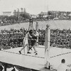 Deux boxeurs se battent sur un ring en plein air entouré d'amateurs.
