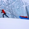 Une femme en ski de fond tire un traîneau devant un mur de glace.