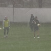 Trois hommes marchent sur un terrain de soccer en pleine tempête de neige.