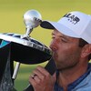 Un homme embrasse un trophée sur lequel se trouve une balle de golf argentée.