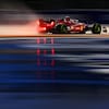 Une monoplace de F1, vue de profil, roule sur un circuit mouillé. On voit le reflet de ses lumières rouges dans les flaques d'eau.