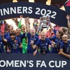 Les joueuses Magdalena Eriksson et Millie Bright tiennent le trophée, entourées de leurs coéquipières, toutes en bleu, et posent pour la photo avec de larges sourires après leur victoire en finale de la FA Cup. 