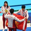 Quatre athlètes en survêtement sont sur le bord d'une piscine et déplie un drapeau de la Chine.