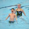 Un jeune nageur artistique et sa partenaire derrière lui font une routine dans une piscine.