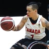 L'athlète, assise dans son fauteuil roulant, tient le ballon dans sa main droite.