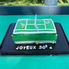 Gâteau en forme de terrain de tennis de couleur verte placé sur une plaque noir