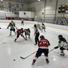 Des joueuses de hockey s'affrontent pendant un match. Une équipe porte un uniforme blanc et vert et l'autre du rouge.