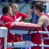 Un entraîneur de boxe, vêtu de rouge, prodigue des conseils en pointant son index sur le front de son athlète dans un ring. 
