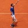 Un joueur de tennis vêtu de bleu et de blanc montre son pouce gauche.