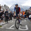 Le cycliste canadien Derek Gee est debout sur son vélo, dans une route pentue en haute montagne.