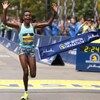 Une femme franchit la ligne d'arrivée d'une épreuve de course à pied, à Boston, et lève les bras en signe de victoire.