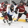 Trois joueuses de hockey tentent de maîtriser une rondelle.
