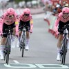 Trois cyclistes dans le maillot rose de l'équipe EF sur leurs vélos de contre-la-montre, le visage crispé par l'effort, approchent la ligne d'arrivée. 