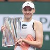 Une joueuse de tennis tient un trophée en verre et sourit.