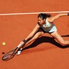 Une joueuse de tennis vêtue d'une robe pastel s'étire pour frapper une balle du revers sur un court en terre battue. 