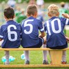 Trois jeunes joueurs de soccer de dos, assis sur un banc.