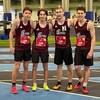 Quatre coureurs portant les uniformes de course sur la piste avec les installations en arrière-plan.