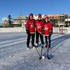 Trois jeunes femmes prennent une photo avec leur bâton de hockey sur une patinoire extérieure.