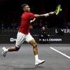 Un joueur de tennis, vêtu de rouge, frappe une balle du coup droit sur un terrain gris à la Coupe Laver à Londres. 