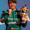 Un pilote heureux, très souriant, tient son trophée et serre le poing droit.