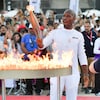 Un homme sourit en tenant une torche olympique au-dessus d'un anneau en flamme.