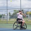 Une joueuse de tennis en fauteuil roulant se prépare à retourner une balle dans les airs. 