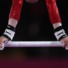 Une gymnaste se tient avec ses bras, tête à l'envers, sur une barre horizontale.